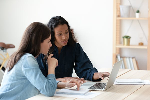 Focused-diverse-female-colleagues-sit-at-desk-in-office