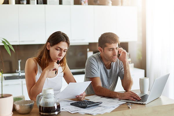 female-reading-attentively-document-and-male-sitting-in-front-of-open-laptop-and-chatting-with-business-partner-over-smart-phone,