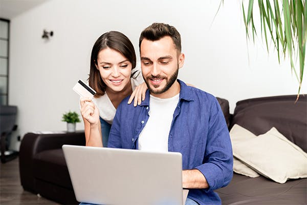Img of young couple in casual clothing sitting on sofa and using laptop and unlimited credit card