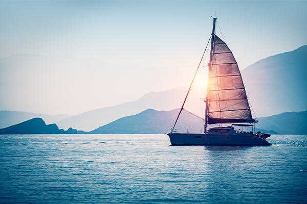 Sailboat-in-the-sea-in-the-evening-sunlight-over-beautiful-big-mountains-background,